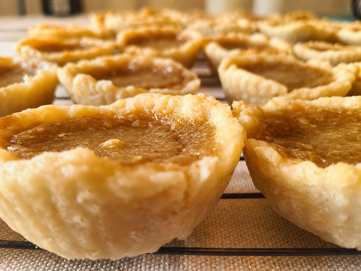 Close-up of homemade butter tarts with golden brown filling on a cooling rack