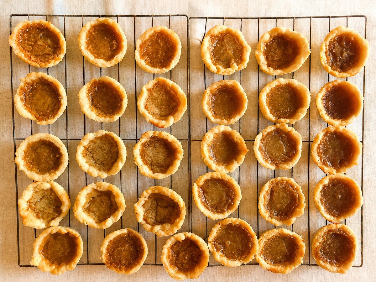 Overhead view of a full batch of homemade butter tarts arranged on a wire cooling rack